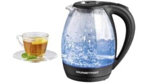 Ein kabelloser Wasserkocher GourmetMaxx 07971 mit kochendem Wasser und schwarzem Griff steht neben einer Tasse Tee, garniert mit einer Zitronenscheibe und Minzblättern auf einer Untertasse.
