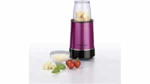 Ein lilafarbener GOURMETmaxx-Standmixer mit gehackten Zutaten darin, daneben eine Glasschüssel mit geriebenem Käse, Kirschtomaten und frischen Basilikumblättern – perfekt für jeden Smoothie-Maker-Enthusiasten.