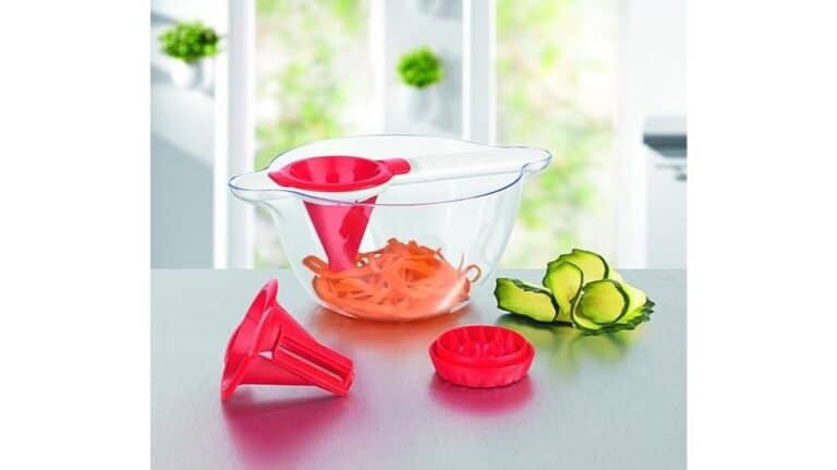 Ein Gourmetmaxx-Spiralschneider mit roten Aufsätzen steht in einer durchsichtigen Auffangschale und präsentiert spiralförmig geschnittene Karotten und Gurkenscheiben auf der Arbeitsplatte.