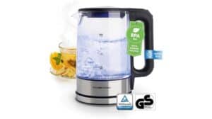 Der GOURMETmaxx Glas-Wasserkocher mit schwarzem Griff kocht Wasser neben einer Tasse Zitronentee. Das BPA-freie Etikett und die Prüfzeichen sind gut sichtbar und machen ihn zu einem Blickfang in jedem Wasserkocher-Testbericht.
